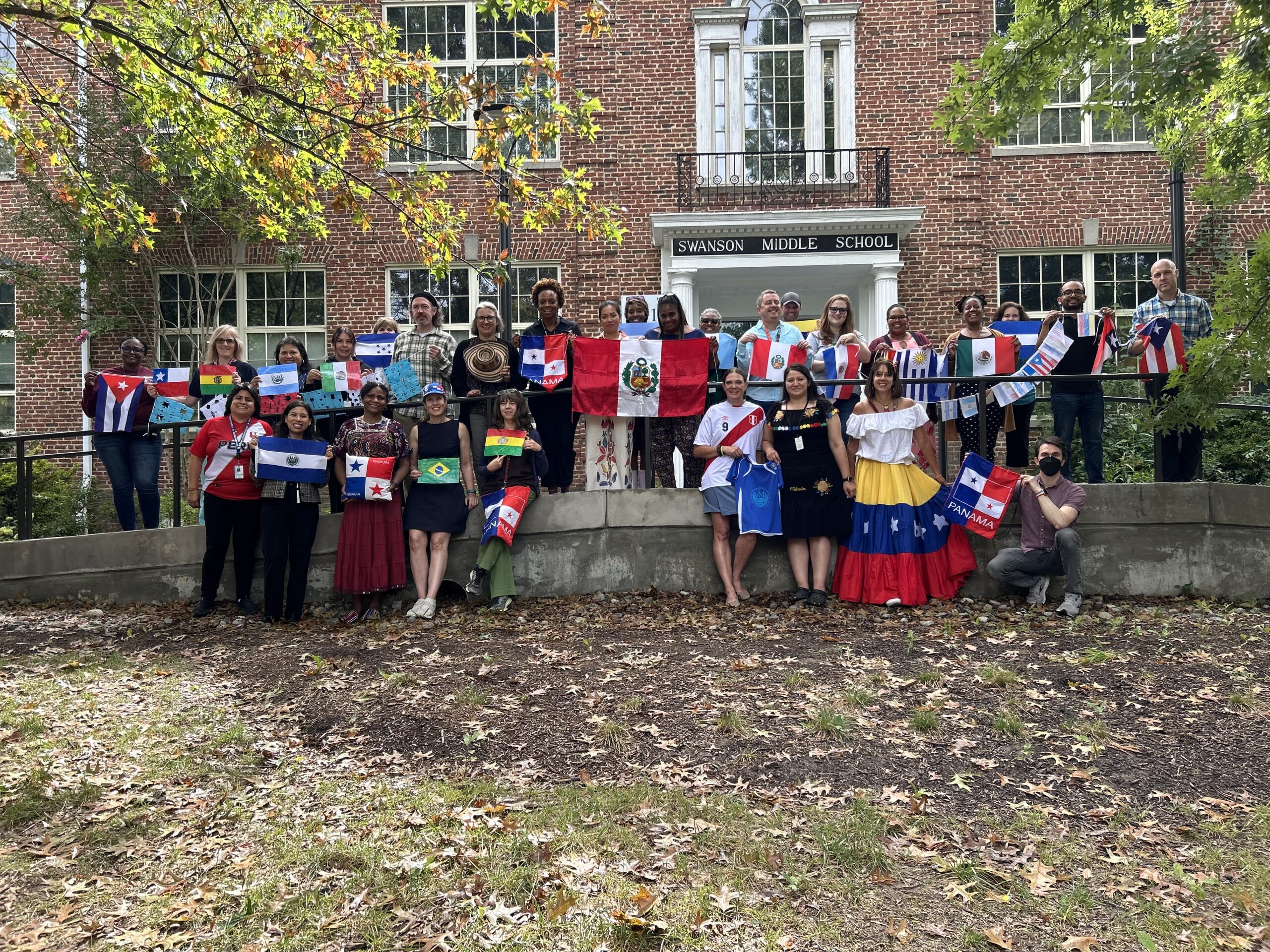 Swanson staff members holding central and south american flags in front of the school