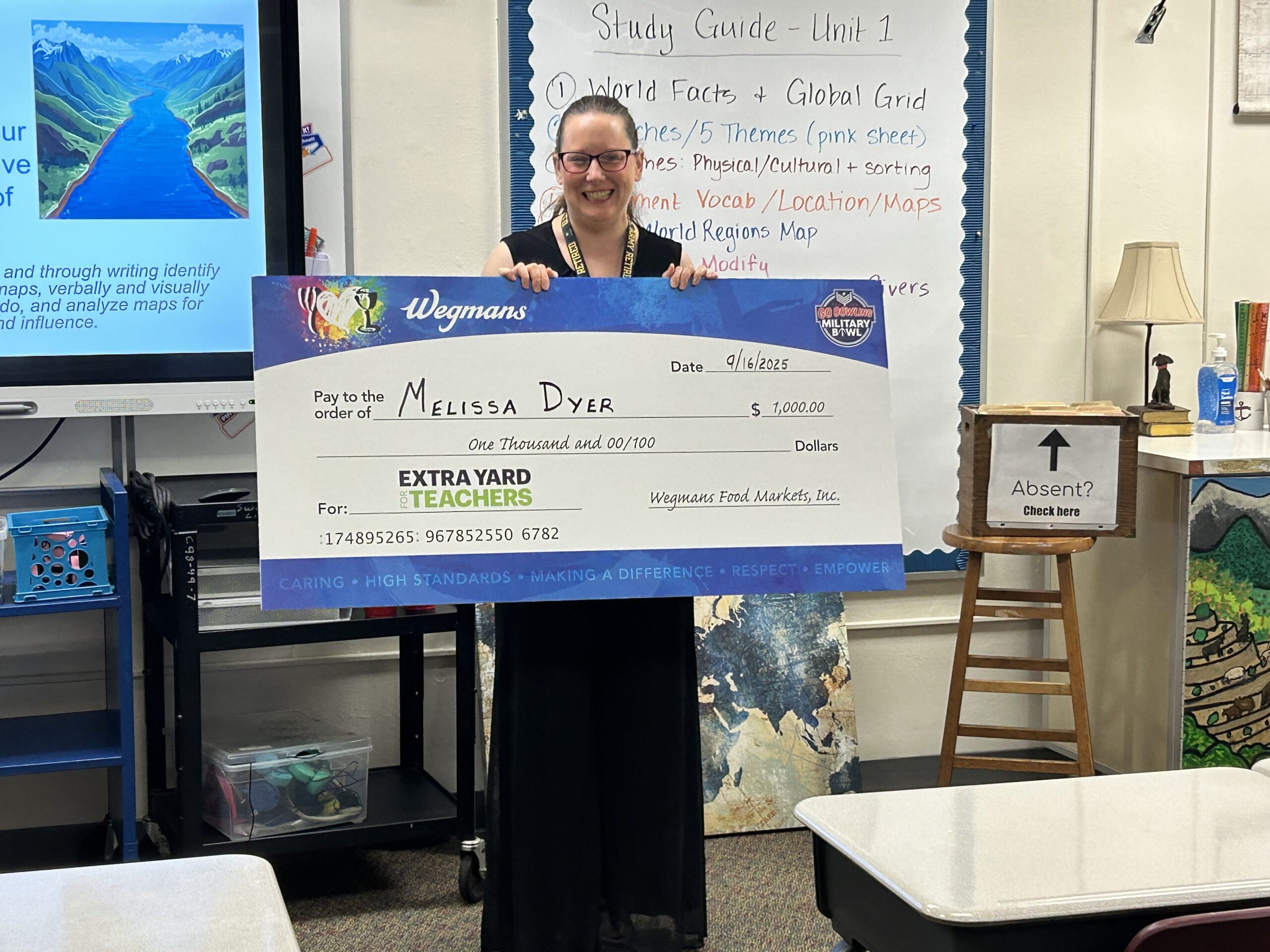 Ms. Dyer holding an oversized check for $1000 in her classroom