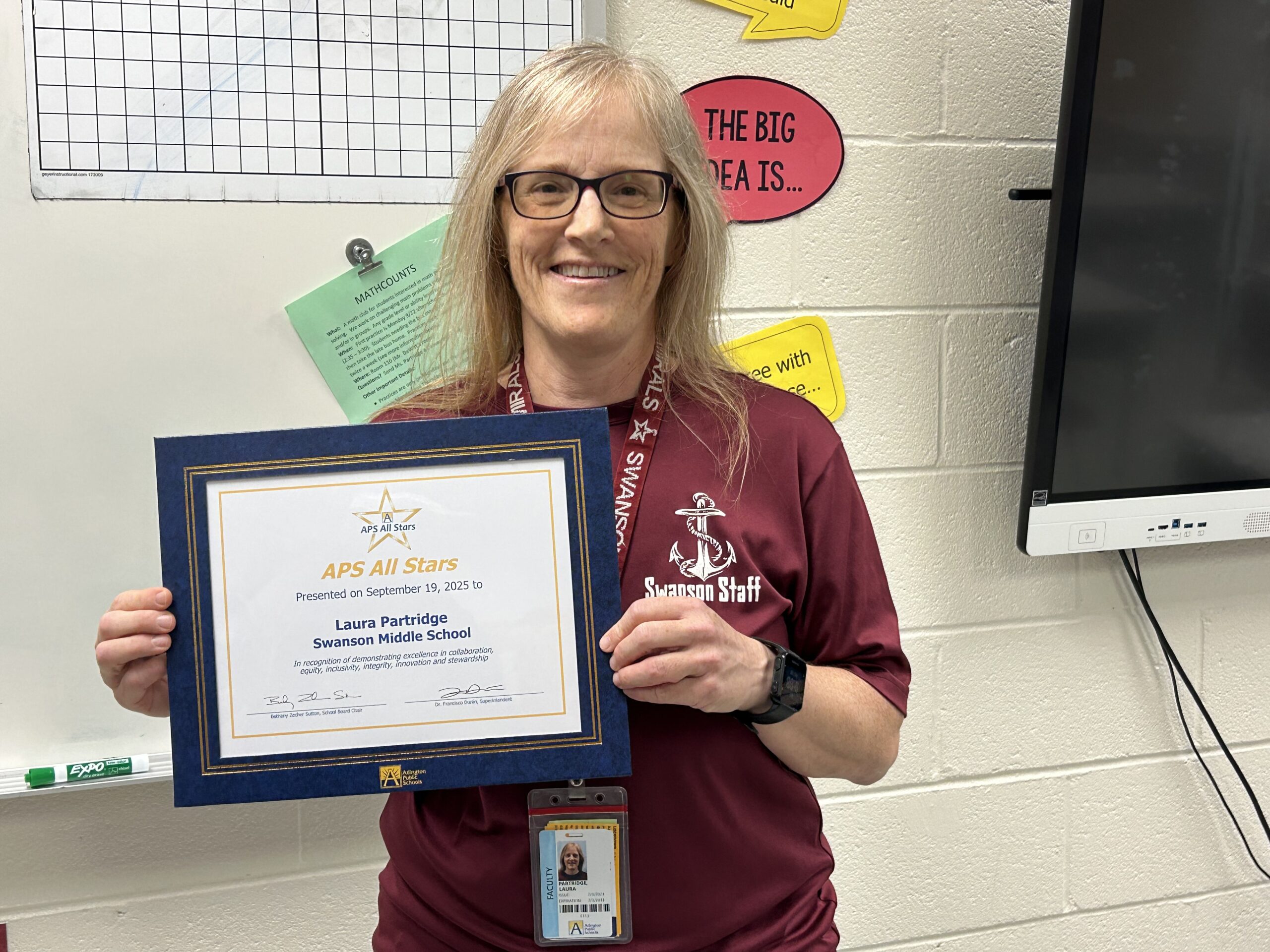 Ms. Partridge holds her certificate for September APS All-STAR in a classroom.